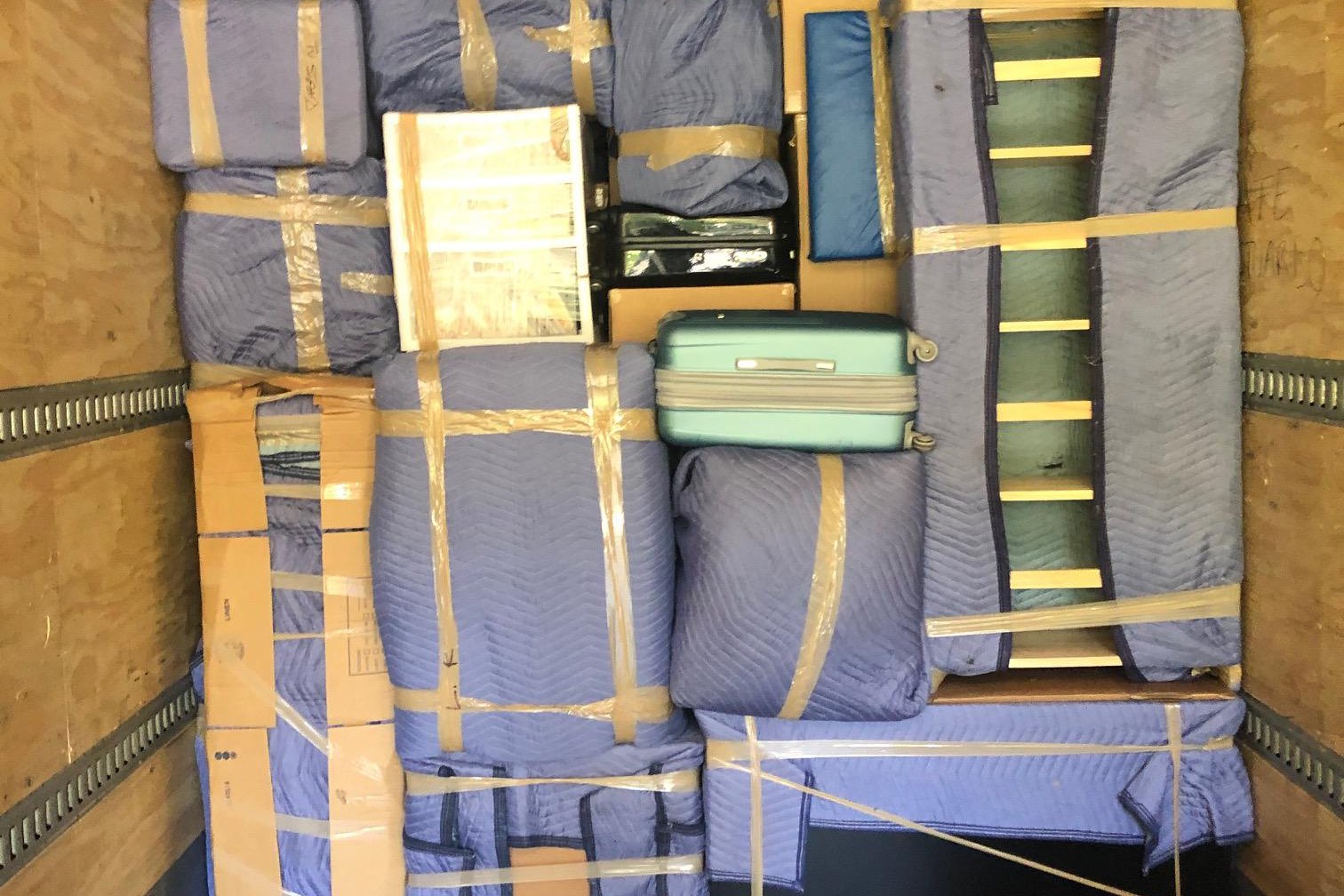 Rear view into a box truck packed with blanket-wrapped furniture, a suitcase and boxes