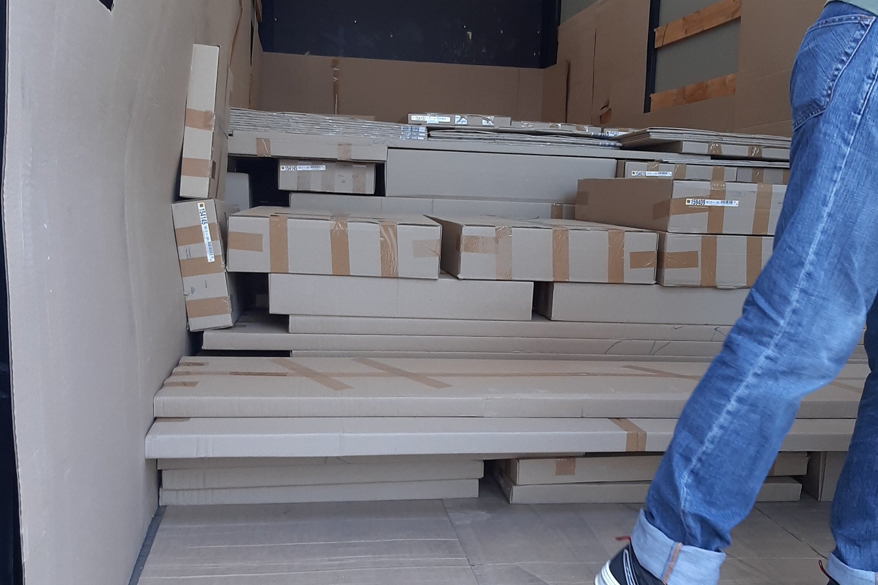 A mover walking past flat-packed furniture boxes laid out inside a box truck