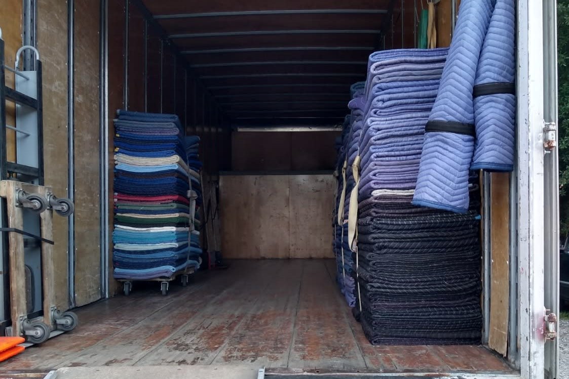 Open box truck with stacks of folded moving blankets, dollies and a loading ramp